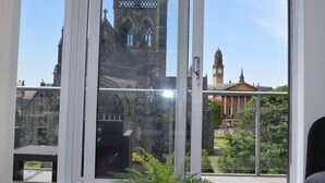 Blick durch ein Fenster auf ein historisches Gebäude mit gotischer Architektur, darunter ein markanter Turm und ein Uhrturm.