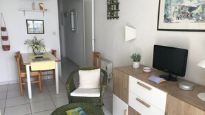 Une pièce moderne et bien éclairée, comprenant une table à manger, des chaises, une petite table ronde, un bureau avec un écran d’ordinateur et une étagère murale agrémentée d’objets décoratifs.