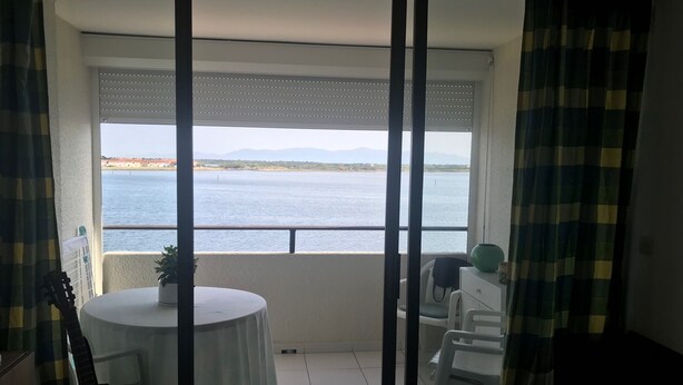 Un balcon avec vue sur la mer, une table avec une plante et une guitare.