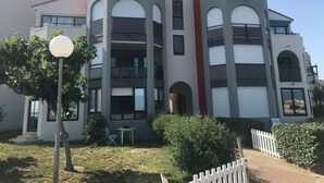 Un immeuble résidentiel à plusieurs étages, doté de balcons, d’un petit patio et d’une clôture blanche en bois.