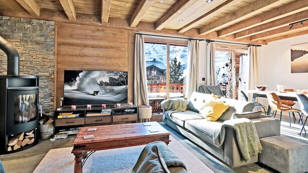 Una sala de estar acogedora con chimenea de piedra, vigas de madera, un televisor grande y un sofá con cojines.