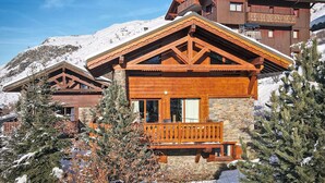 Una cabaña de madera con balcón, rodeada de árboles nevados y montañas.