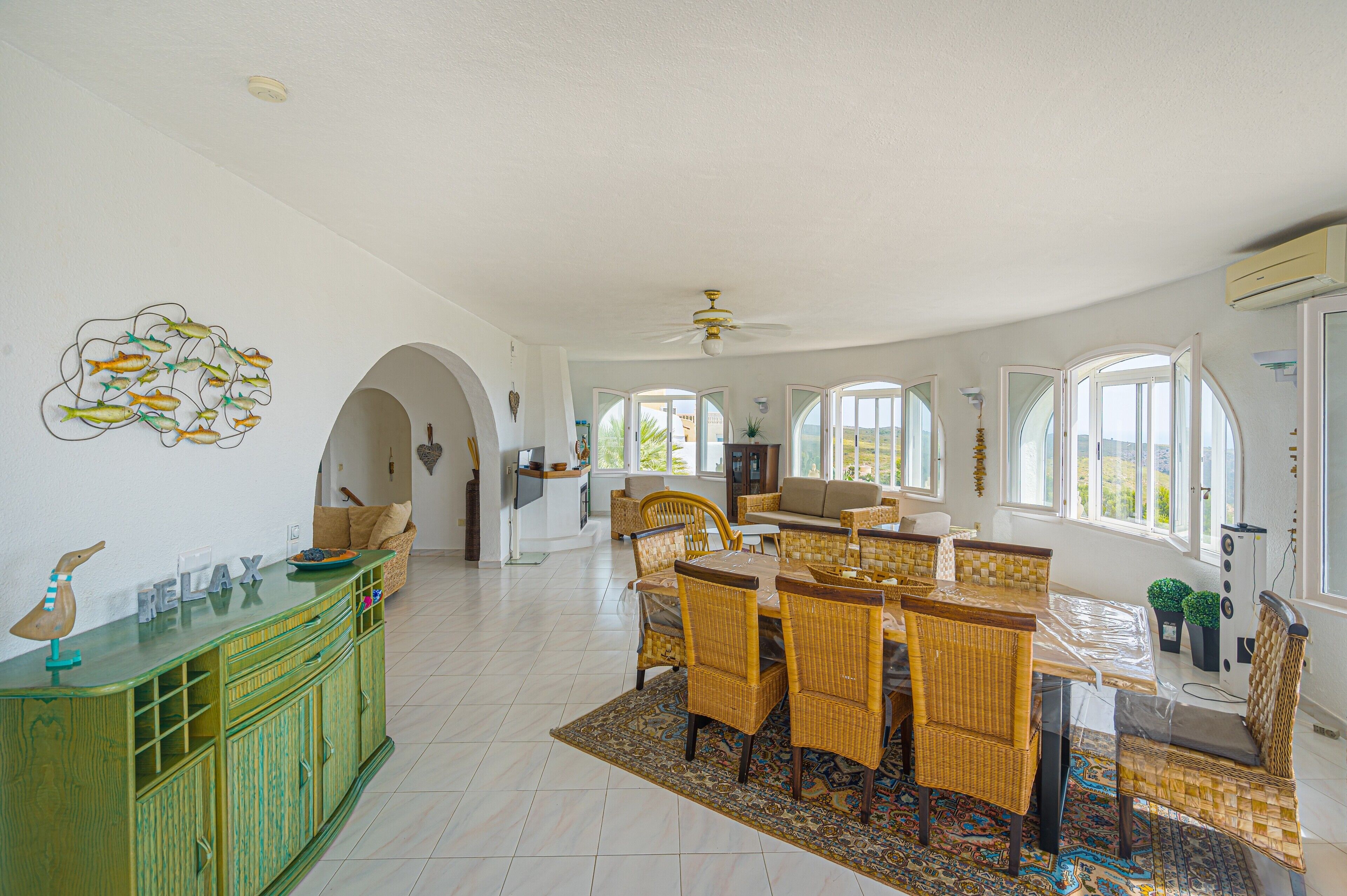 A spacious dining area with a large table and chairs, a green cabinet with decorative items, and a ceiling fan.