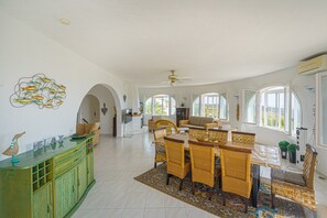 A spacious dining area with a large table and chairs, a green cabinet with decorative items, and a ceiling fan.
