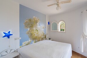 A bedroom with a bed, a ceiling fan, a wall-mounted star light, and a window with a view.
