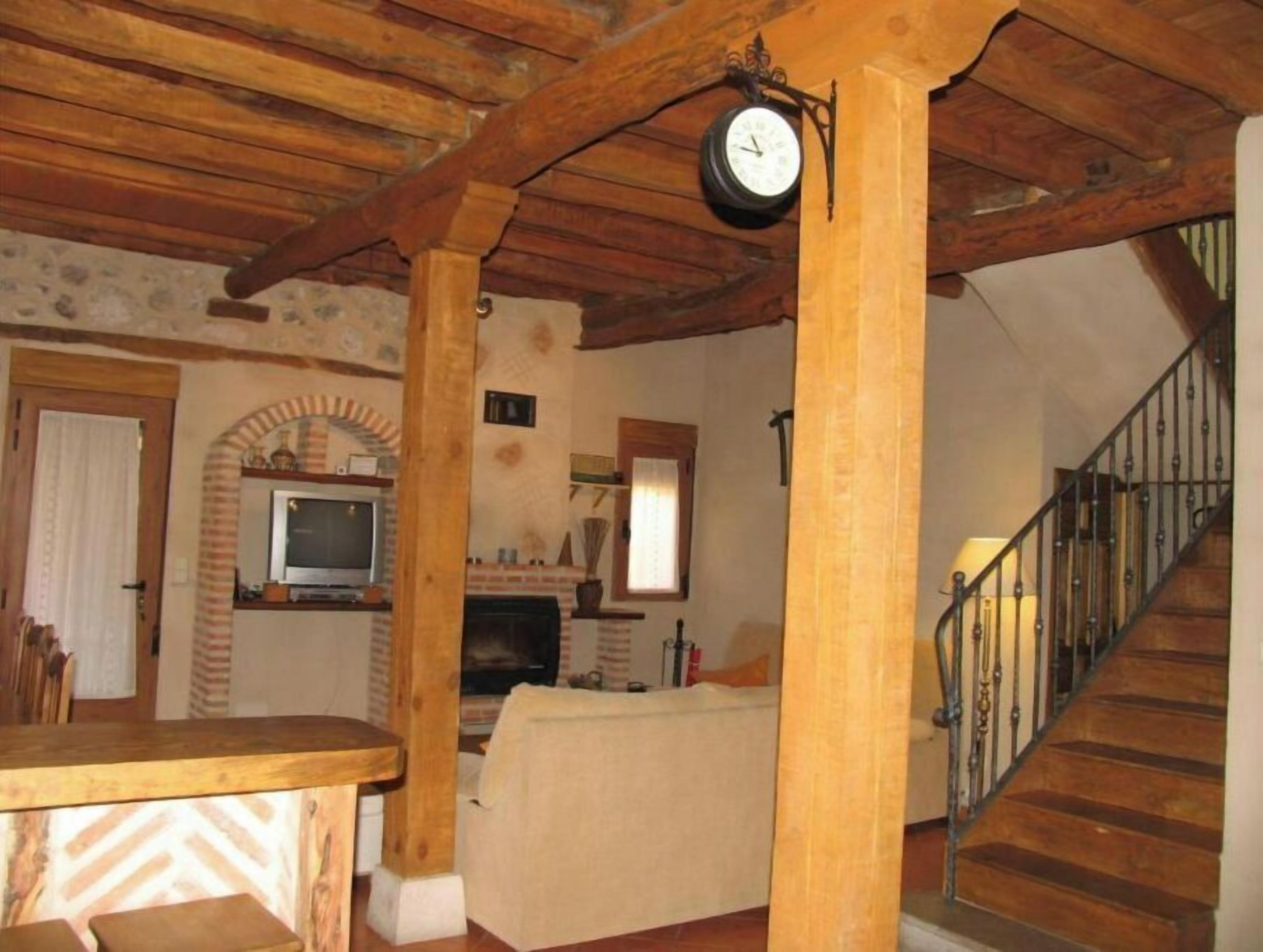 Ein rustikales Interieur mit freiliegenden Holzbalken, einem Kamin, einem Fernseher und einer Treppe.