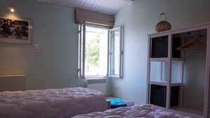 A bedroom with two beds, a window, a wardrobe, and a hanging light fixture.