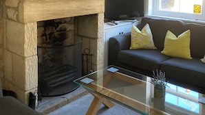Un salon avec une cheminée en pierre, une table basse en verre, un canapé avec des coussins et un téléviseur posé sur un meuble.