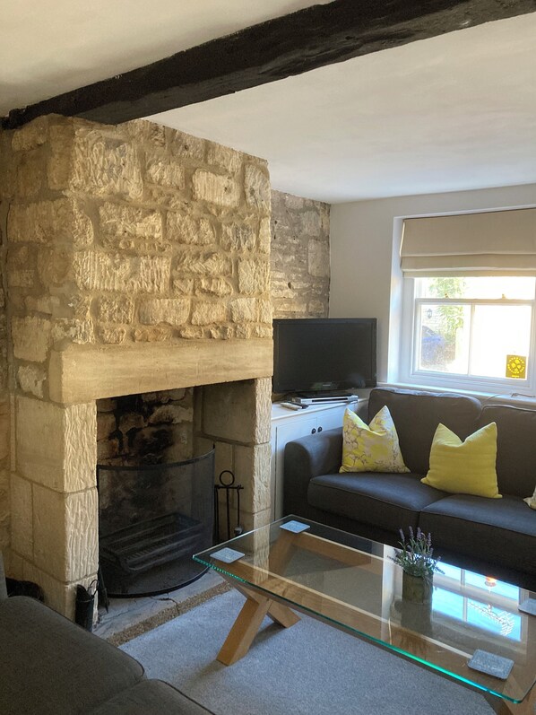 A living room with a stone fireplace, a glass coffee table, a sofa with cushions, and a television on a stand.