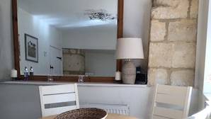 Un coin repas comprenant une table ronde, quatre chaises, un panier en osier, une lampe et un mur en pierre.