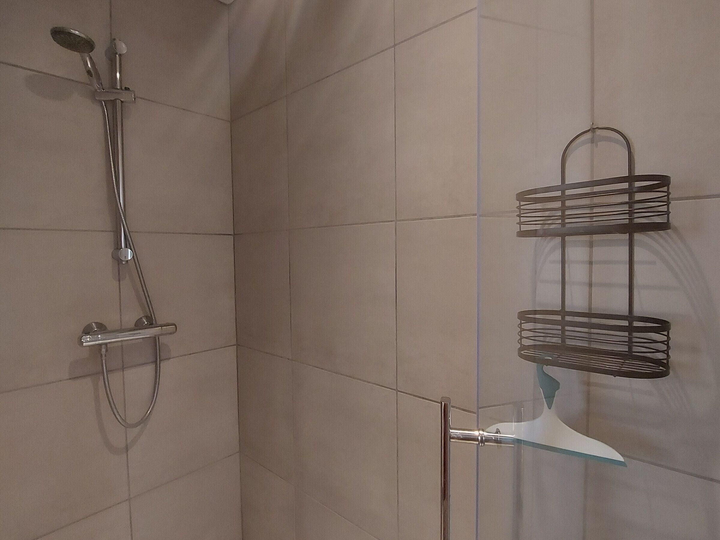 Eine Dusche mit Handbrause und wandmontiertem Wasserhahn. Ein Metallhandtuchhalter mit zwei Halterungen für Handtücher.