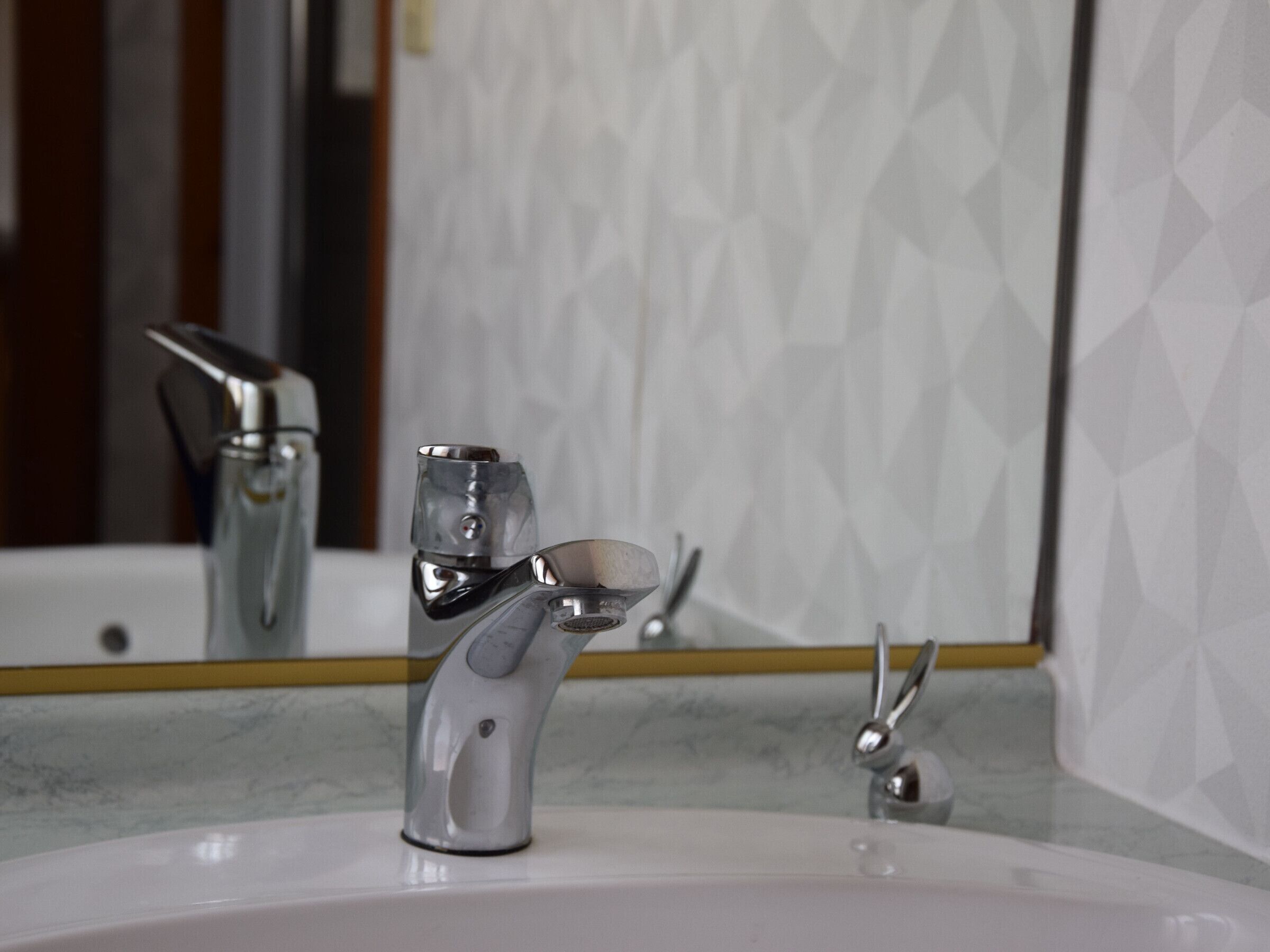 Une salle de bain moderne avec un robinet chromé, un miroir et un comptoir en marbre.