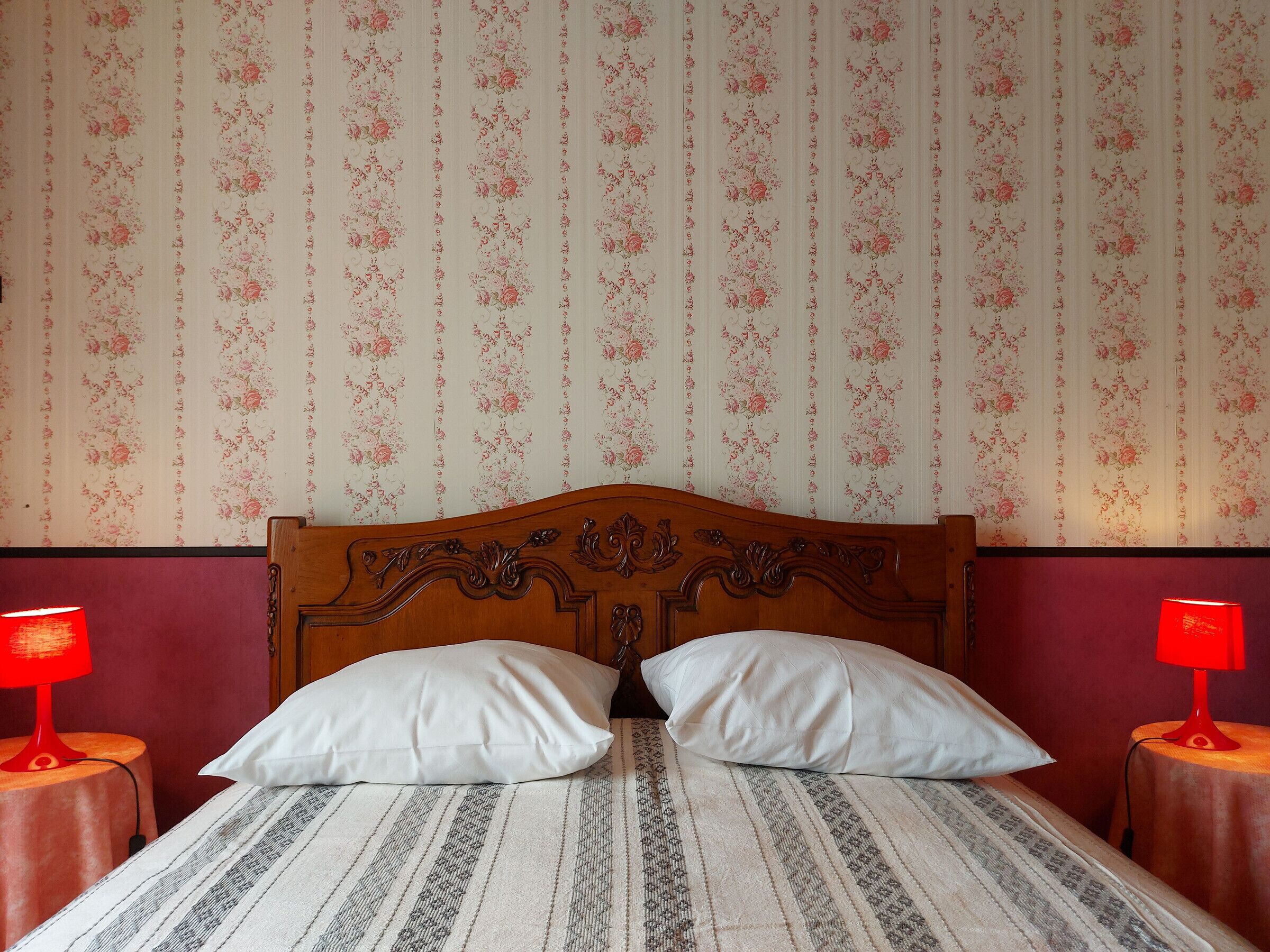 A bedroom with a wooden headboard, two white pillows, a striped bedspread, and floral wallpaper.