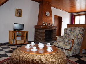 A cozy room with a fireplace, a television, a floral armchair, and a round table with teacups.