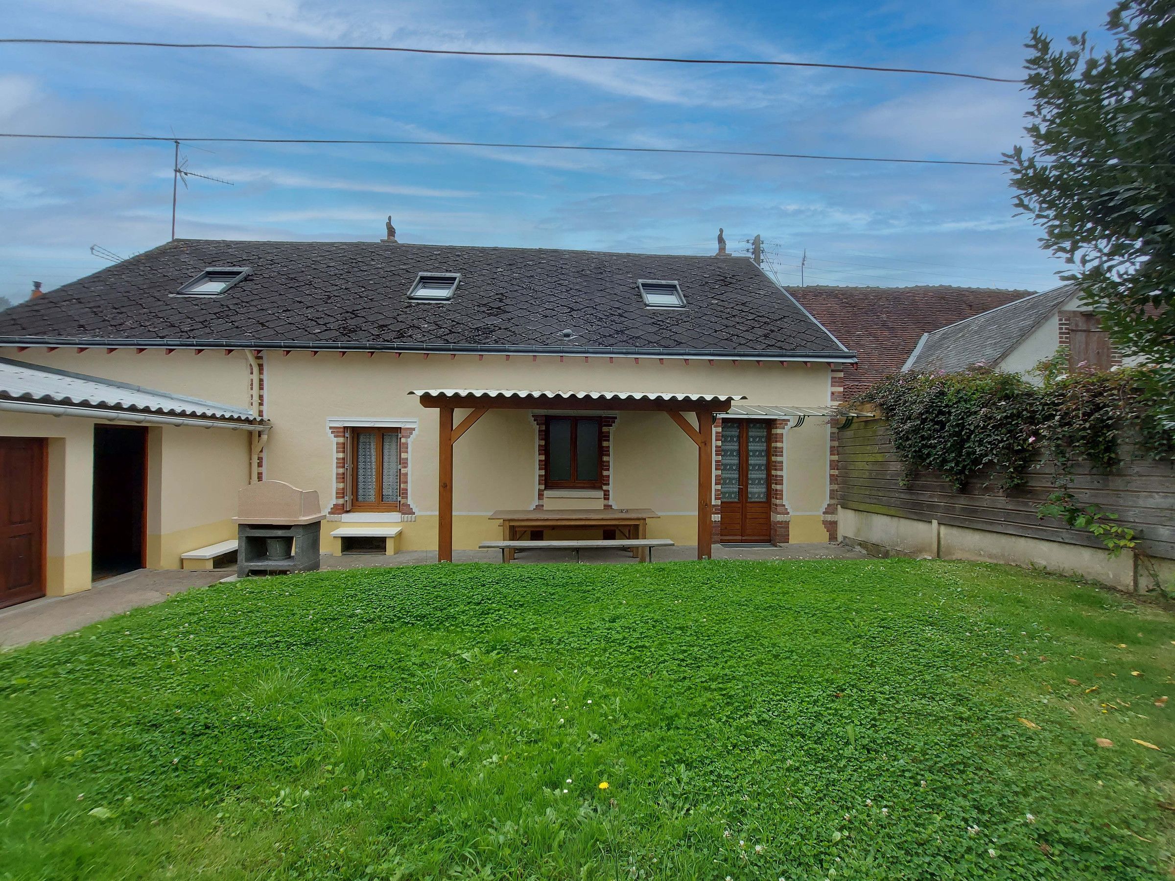 Una casa a due piani con tetto spiovente, un portico coperto e un piccolo giardino antistante.