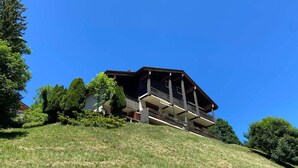 A two-story building with a balcony on the upper floor, surrounded by greenery and a clear blue sky. - Charming 3-room with mezzanine for 6 pers, south balcony and parking in La Clusaz (La Clusaz)