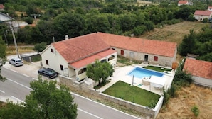 A two-story house with a red-tiled roof, a swimming pool, and a well-maintained lawn. - Cozy house in the village (Siveric)