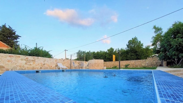 A swimming pool with blue tiled edges, surrounded by stone walls and greenery. - Cozy house in the village (Siveric)