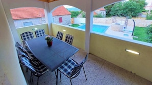 A covered patio area with a table and chairs, a view of a swimming pool, and a stone building in the background. - Cozy house in the village (Siveric)