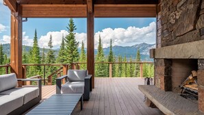 Une terrasse couverte avec une cheminée en pierre, des sièges d’extérieur et une vue sur les montagnes.