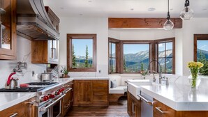 Une cuisine moderne avec des meubles en bois, un grand îlot central et une vue sur les montagnes grâce à de grandes fenêtres.