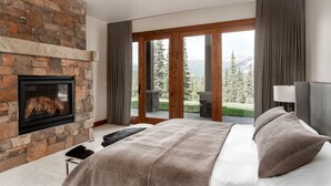 Une chambre dotée d’une cheminée en pierre, d’un grand lit et offrant une vue sur un paysage montagneux grâce à de grandes portes vitrées.