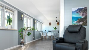 A modern living room with a black leather sofa, a dining area with white chairs, and a kitchen in the background. - Apt. WEITER BLICK - Welcome, make yourself comfortable! (Insel Poel / OT Neuhof)