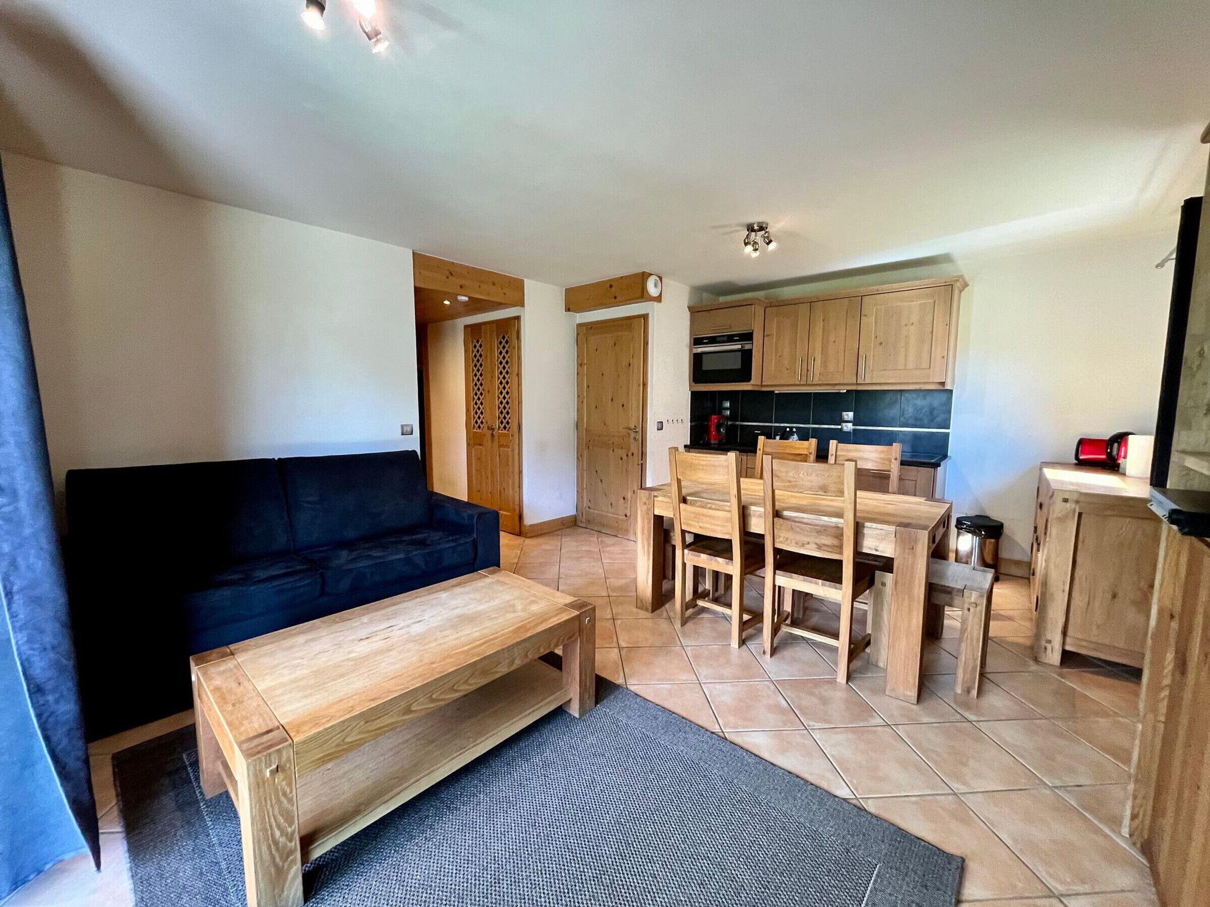 A compact living space with a sofa, a dining table with chairs, a kitchen area with wooden cabinets, and a small television.
