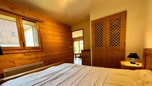 A bedroom with a wooden slatted door, a bed with white bedding, and a nightstand with a lamp. - T2 Apartment with Large Terrace and Pets Allowed (Samoëns)