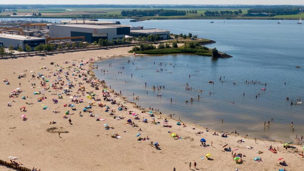 Een strand met mensen die zonnen en zwemmen, omringd door gebouwen en een wateroppervlak.