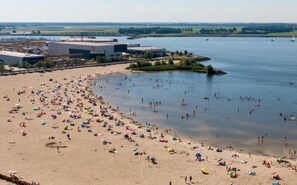 A beach with people sunbathing and swimming, surrounded by buildings and a body of water. - Hot tub! Next to the beach (Lemmer)