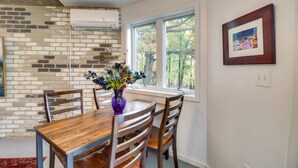 A dining area with a wooden table and chairs, a vase with flowers, a brick wall, and a window with a view of trees.