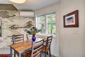 A dining area with a wooden table and chairs, a vase with flowers, a brick wall, and a window with a view of trees. - Renovated Studio on 5 Acres - Near Vineyards! (Crozet)