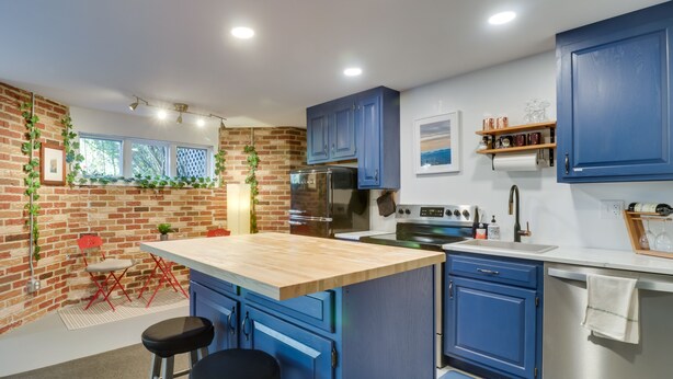 A modern kitchen with blue cabinets, a wooden island, and a brick wall.