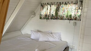 A bedroom with a sloped ceiling, a bed with white bedding, and a window with tropical curtains. - Reed hut / pile dwelling on Lake Neusiedl (Ruster Bucht)