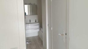 Un corridoio stretto che porta a un bagno con lavandino bianco, uno specchio e due portasciugamani.