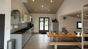 A modern kitchen with a wooden ceiling, a built-in stove, and a dining area with a wooden table and bench.