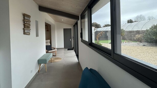 A modern hallway with a bench, a door, and a window with a view of a greenhouse.