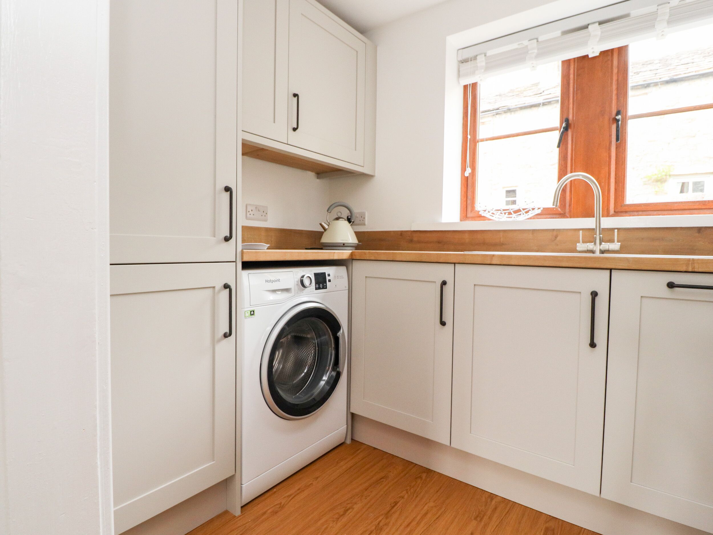 A compact kitchen with white cabinets, a washing machine, a wooden countertop, and a window with a view of the outside.