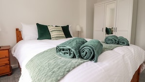 A neatly made bed with green and white bedding, a wooden nightstand, a white wardrobe, and a lamp on the bedside table. - Top House (Settle)