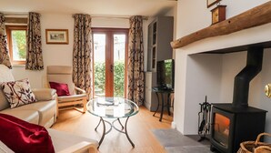 A cozy living room with a sofa, armchair, and a glass coffee table. There's a fireplace with a chimney, and a television on a stand. - Top House (Settle)