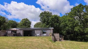A rustic cabin with a large open garage, surrounded by a grassy yard and dense trees.