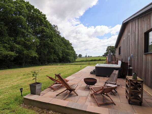 Een terras buiten met lounge fauteuils, een jacuzzi en een vuurkorf.