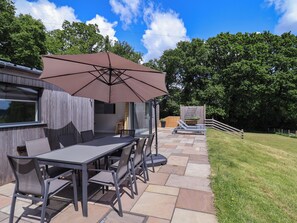 Een terras buiten met een tafel, stoelen, een grote parasol en een barbecue.