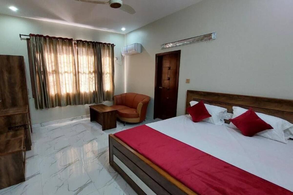 A bedroom with a bed, a chair, a small table, a wardrobe, and a window with curtains.