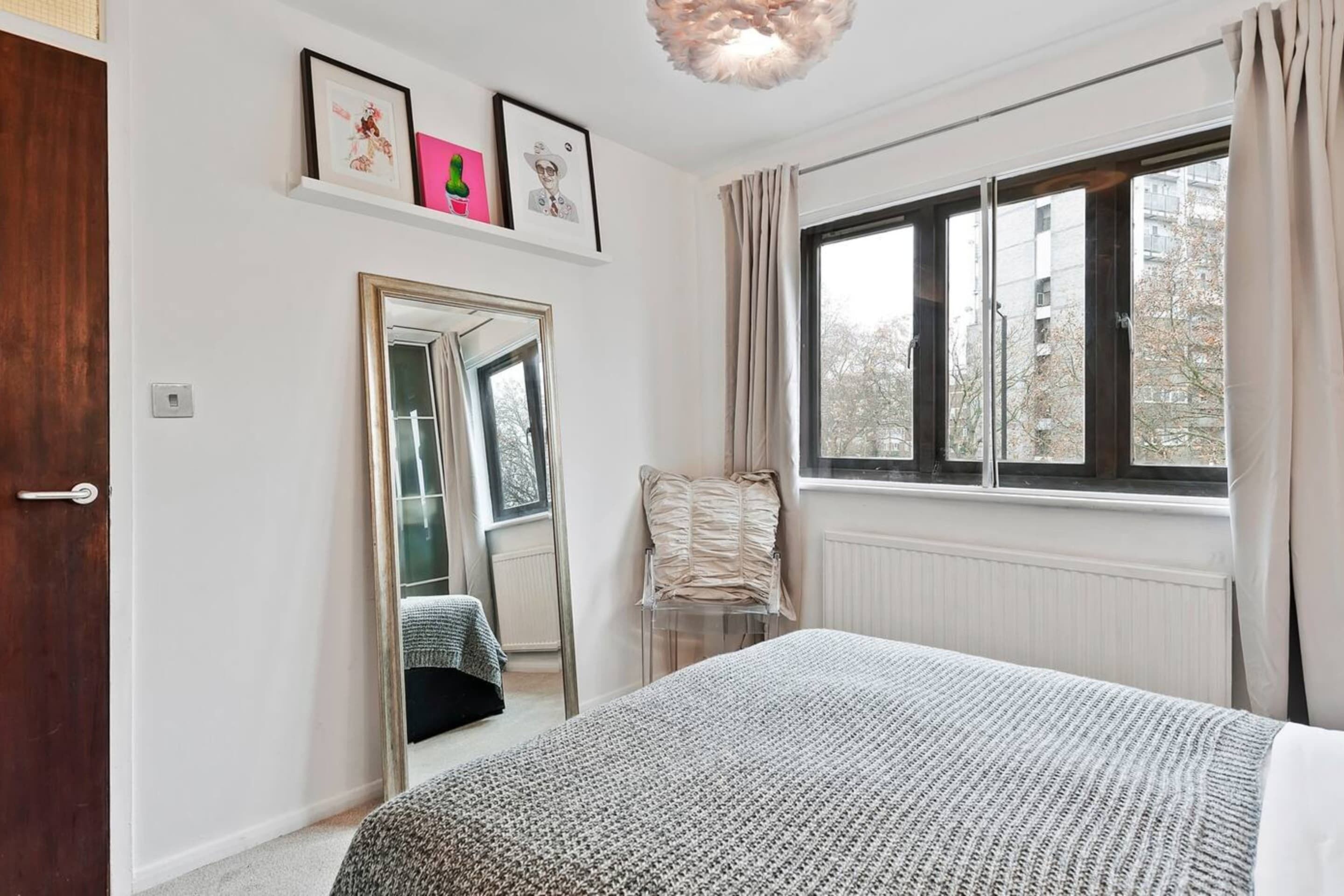 Une chambre à coucher avec un grand lit, un miroir, une fenêtre avec des rideaux et un radiateur.