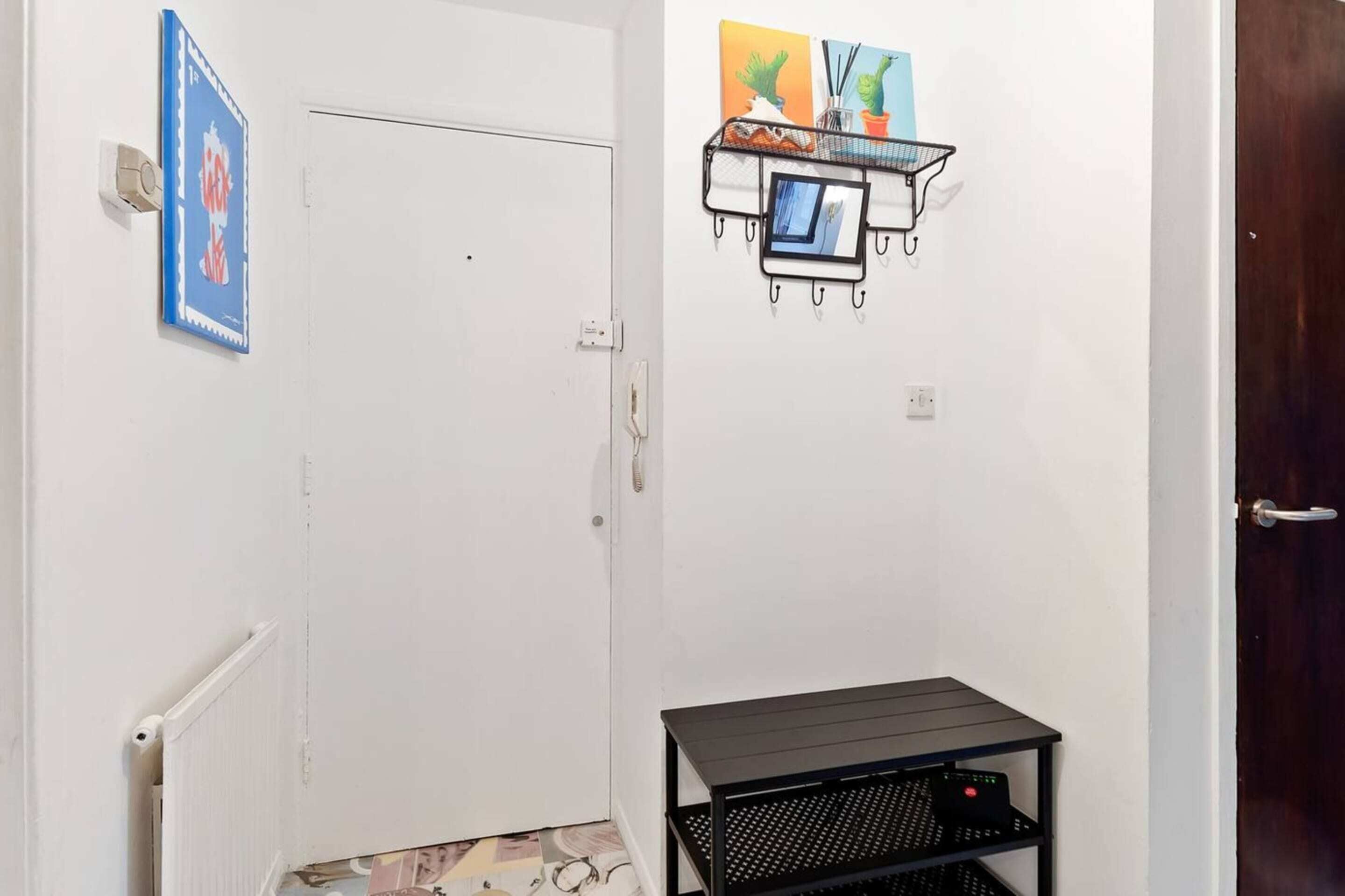 A hallway with a white door, a black metal shelf with a picture frame, and a small black table.