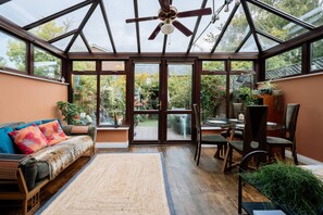 A conservatory with a ceiling fan, a sofa with colorful cushions, a dining table with chairs, and a view of the garden outside. - Charming 2 Bedroom Home in Rathmines Dublin (Dublin)