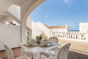 Tavolo bianco apparecchiato all'aperto con vista su un edificio bianco e il mare.