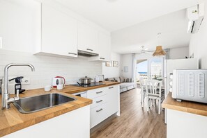 Una cucina moderna con mobili bianchi, un piano di lavoro in legno, un lavello in acciaio inossidabile e un'area pranzo con sedie e tavolo bianchi.